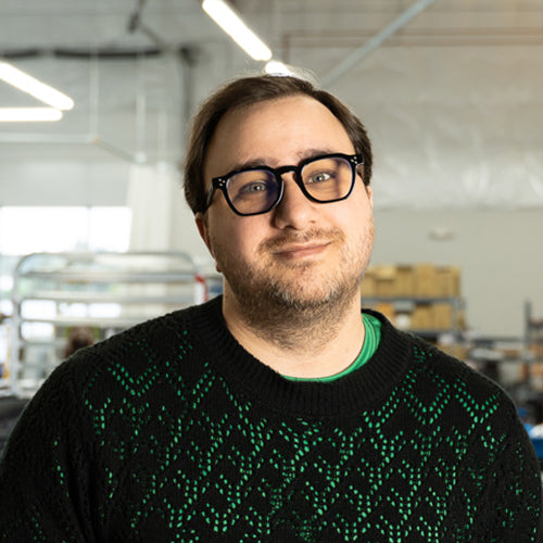 Man wearing glasses and a black sweater with green patterns in an indoor setting