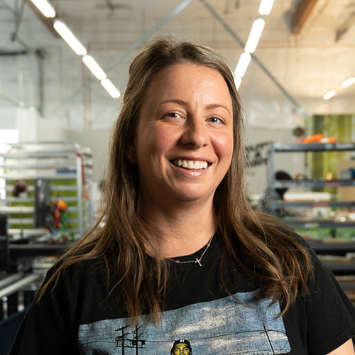 Woman wearing a black apron with a graphic design, smiling in an indoor setting.