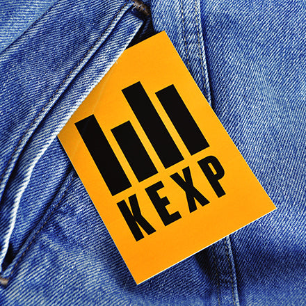Orange tag with black text 'KEXP' attached to a blue denim jacket.