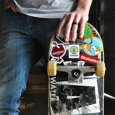 Person holding a skateboard with multiple stickers on a blurred background