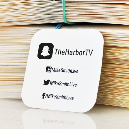 White square tag with social media handles on a stack of papers