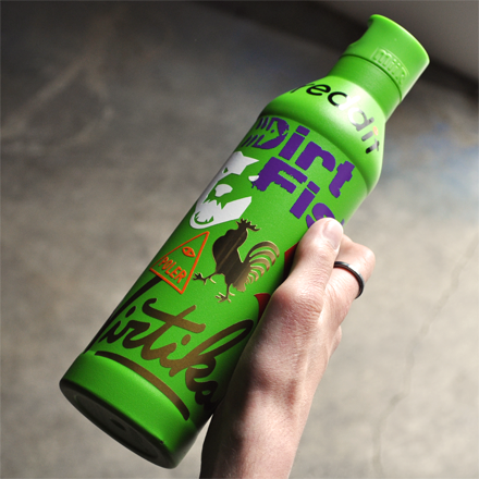 Green bottle with 'Dirt Fish' branding held by a person against a gray background